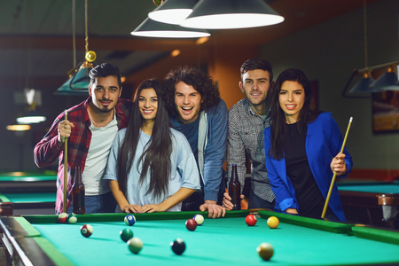 Friends play billiards. A group of young people playing fun billiards.の販売画像