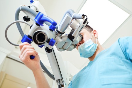 Male dentist looking through a microscope in a dental office.の写真素材