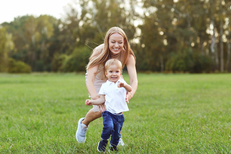 Running adorable boy with loving mother on green meadow in summer park having fun togetherの写真素材