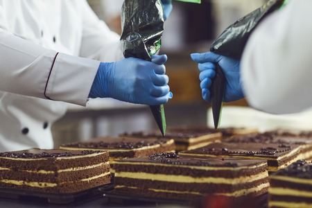 A confectioner decorates cream from a bag on a chocolate cake on a table in a bakery.の写真素材