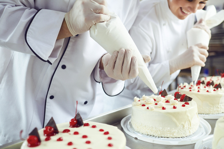 Two pastry chefs decorate a cake from a bag in a pastry shop.の写真素材
