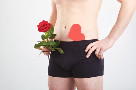 The concept of sex, lover. A man in black underwear holds rose and red heart in his hands.の写真素材