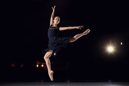 Ballerina in a black suit is jumping on a black background on scene.の写真素材