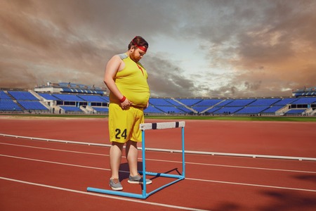 Fat man in sportswear stands in front of a barrier on a track stadium. Winner concept success obstacle problem.の写真素材