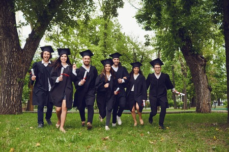 A group of graduates with scrolls in their hands are smiling against the background of the...