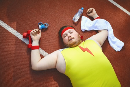 Fat lazy man sleeps tired lies on the track in the stadium. The concept of losing weight, diet. Top...