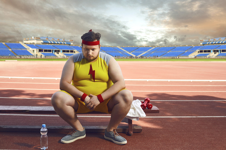 Fat sad man sitting in a stadium after training. The concept of sports, weight loss, diet.の写真素材