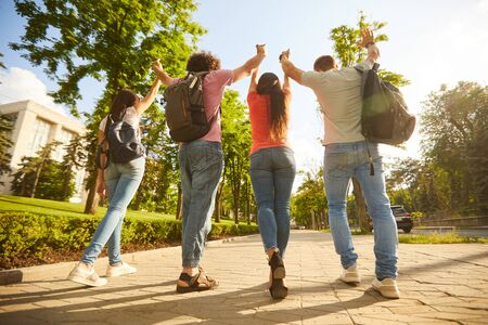 A group of happy young people raised their hands up at sunset on the street sunset sity. Friends in...