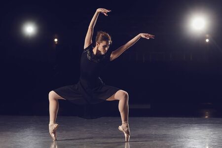Woman ballet dancer in black dress posing on black background.