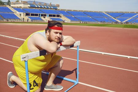 Fat funny man sitting down resting on the track in the stadium.の写真素材
