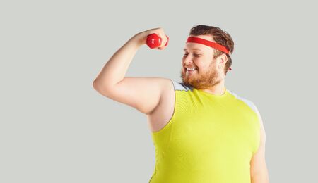 The fat funny man with a beard with dumbbells goes in for sports on a gray background.の写真素材