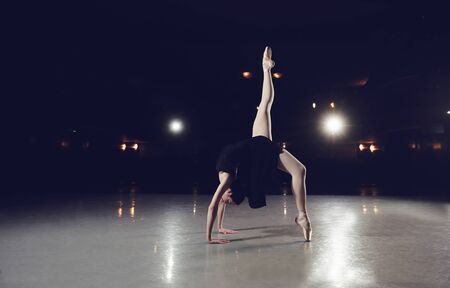 Ballerina in a black suit is jumping on a black background on scene.