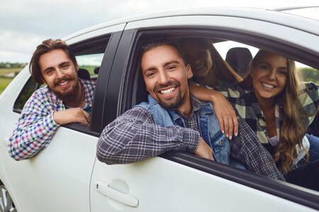 A group of happy friends travelers are driving in a car on road.の写真素材