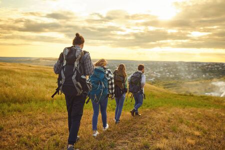 Young people with backpacks stand in the forest from behind. Tourists on the tourist route.