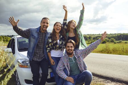 A group of friends travelers laughing near the car by the road.