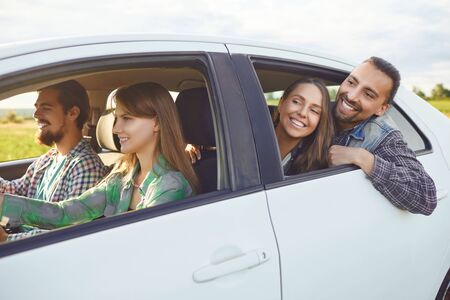 A group of happy friends travelers are driving in a car on road.の写真素材