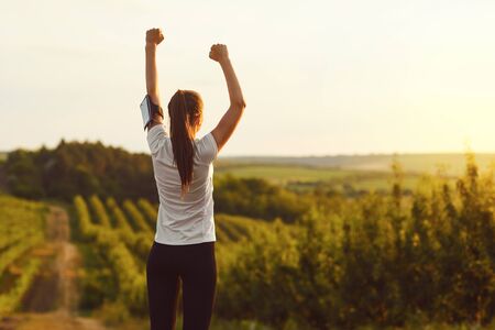 Athletic girl raised her hands up at a training on the nature on the morning. Active lifestyle.の写真素材
