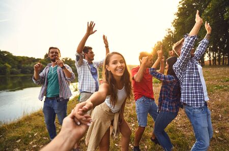 Friends on a picnic dance on the lake in the evening at sunset. People have fun outdoors for the weekend in the summer in autumn.の写真素材
