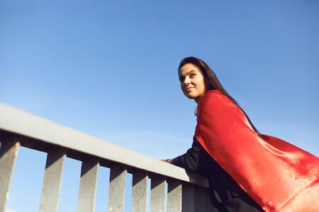 Successful superhero businesswoman in a red cape on a background of blue sky in the city.の写真素材