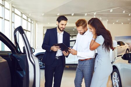 A couple buys a car in a car showroom. A man signs a car rental agreement.