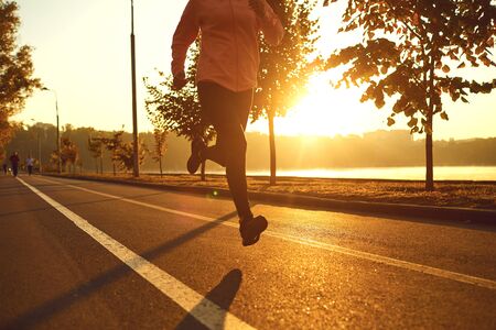 Runner runs on the road in the sun at sunset in an autumn park. Jogging for health.