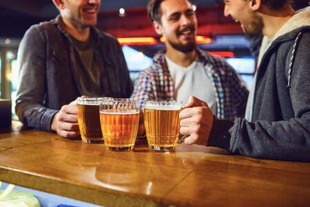 Friends with glasses of beer in hand are laughing at the bar. Meeting friends in the pub.の写真素材