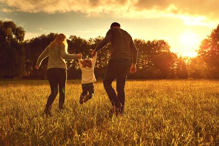 Happy family walks on the park at sunset.Back view. Parents with a child in nature. Children Protection Day.の写真素材
