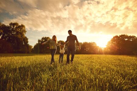 Happy family walks on the park at sunset. Parents with a child in nature. Children Protection Day.の写真素材
