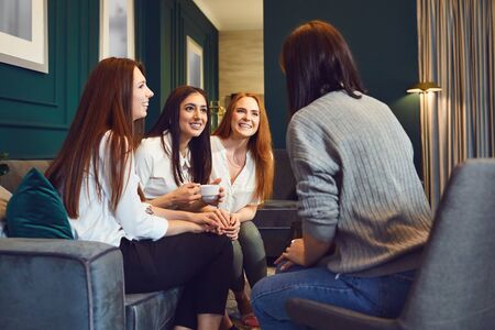 Young content women sitting on sofa at home having tea and chatting in leisureの写真素材