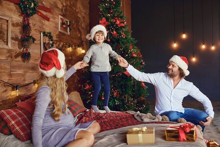 Happy pregnant woman with man holding hands of jumping boy while sitting with Christmas presents on...