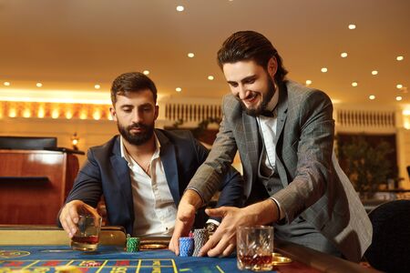 Group man friends in a suit is sitting at table roulette playing poker at a casino.
