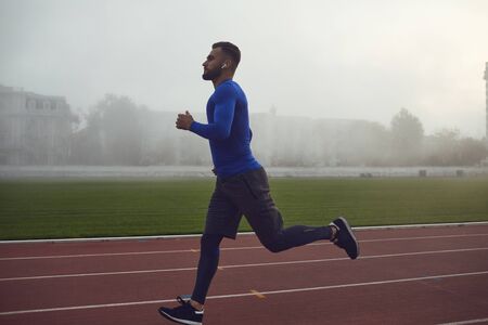 A young athlete runs on a stadium in the fog. Jogging during training.Jogging. Health. Healthy lifestyle.の写真素材