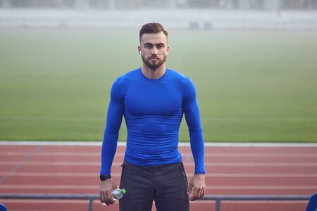 A male athlete with a beard in training stands at the stadium in the fog. Health. Healthy lifestyle.