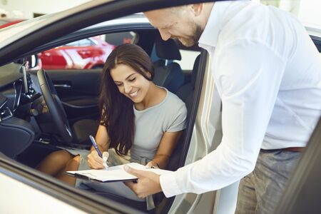 A young woman buys a car in a car showroom. A man signs a car rental agreement.の写真素材