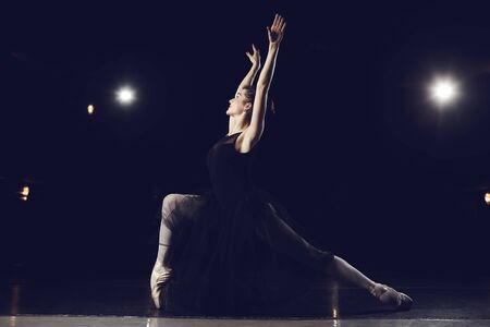 Woman ballet dancer in black dress posing on black background.の写真素材