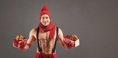 Athletic man with gifts smiling at christmas over gray background.