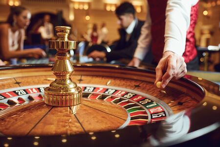 Hand of a croupier with a ball on a roulette wheel during a game in a casino. Gambling betting game poker roulette casino concept.の写真素材