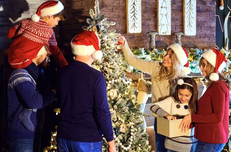 Family in Santas hats decorates the Christmas tree at home on Christmas. Celebration of the new year...
