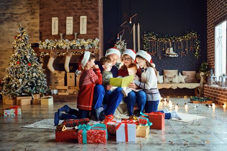 Grandparents reading a book with a child in the room with the Christmas tree on Christmas Day.の写真素材