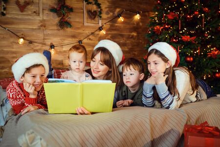 Mother reads a book with children lying on the bed in the room with the Christmas tree at Christmas.の写真素材