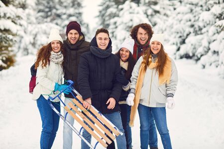 Friends smiling at the camera with sleds in their hands on the snow on the nature in winter