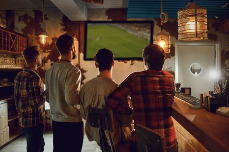 A group of people watching tv football in a sports bar. Fans cheerfully cheer in a restaurant, drink beer.