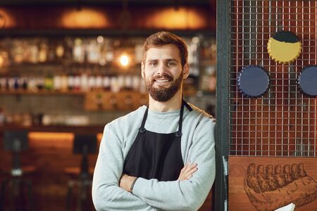 Bearded smiling barman waiter standing on the background of a restaurant pub bar.の写真素材