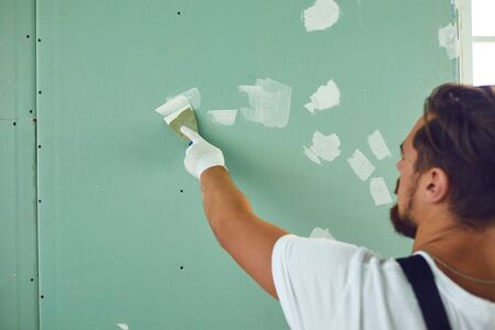 Worker builder plasterer plastering a wall of drywall at a construction site indoors. Back viewの写真素材