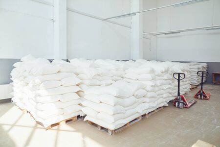 Folded white bags on pallets in factory storage. Bags of rice sugar flour corn cement in storage.