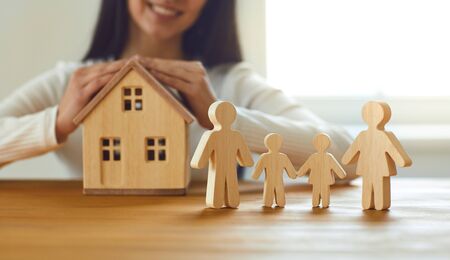 Family home insurance mortgage rental construction loan concept. Womans hands with a model of the house and figures of seven people on the table against the background of the window.の写真素材