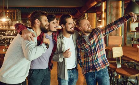 Portrait of friends at a bar pub. A group of men take a selfie on the phone in a restaurant.の写真素材