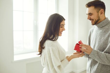 The guy makes a marriage proposal to the girl. Smiling man gives a marriage proposal ring on the background of a bright window in the room.の写真素材