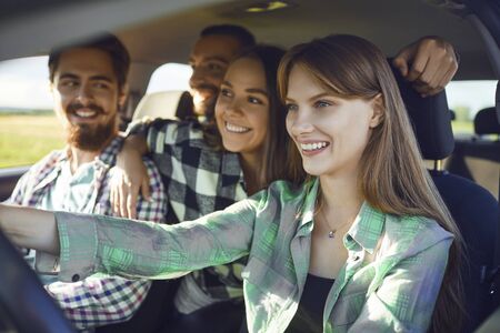 A group of happy smiling friends travelers are driving in a car on road.