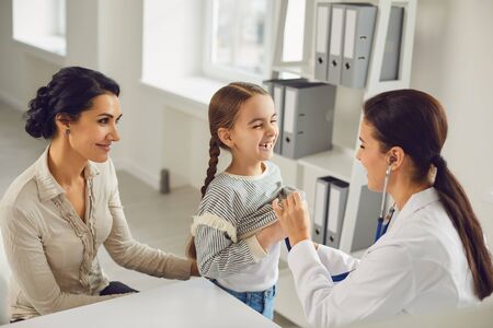 A woman pediatrician makes a setoscope examination to a child girl with mom in a clinic office. Medical care examination care care medicine insurance.の写真素材